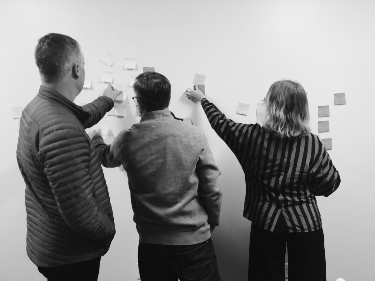 Three Unico employees reach over one another to place sticky notes on a wall during a brainstorming session