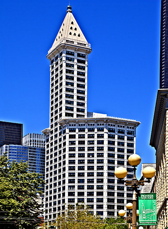 The Smith Tower, a historic 38-story building with neoclassical architecture, in front is a decorative lamp post with a Pioneer Square banner attached